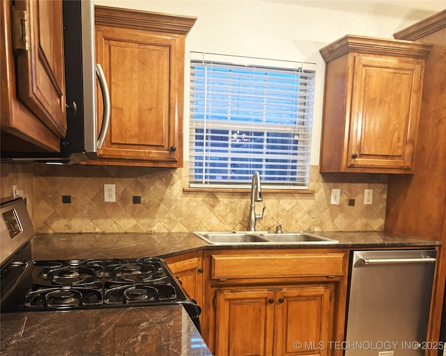 kitchen with stainless steel appliances, brown cabinetry, dark countertops, and a sink