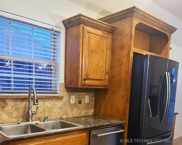 kitchen with decorative backsplash, dark countertops, brown cabinets, refrigerator with ice dispenser, and a sink