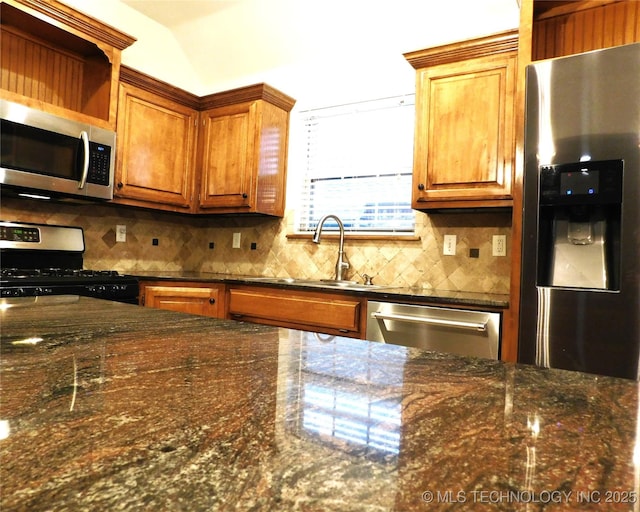 kitchen featuring stainless steel appliances, dark stone countertops, a sink, and decorative backsplash