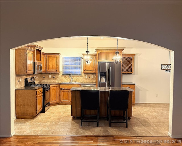 kitchen with arched walkways, tasteful backsplash, appliances with stainless steel finishes, a kitchen island, and a sink