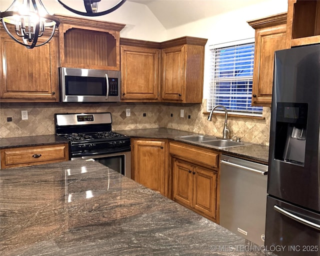 kitchen with stainless steel appliances, a sink, vaulted ceiling, backsplash, and brown cabinetry