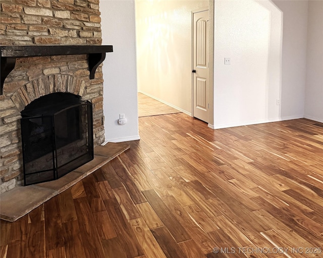 unfurnished living room featuring a stone fireplace, baseboards, and wood finished floors