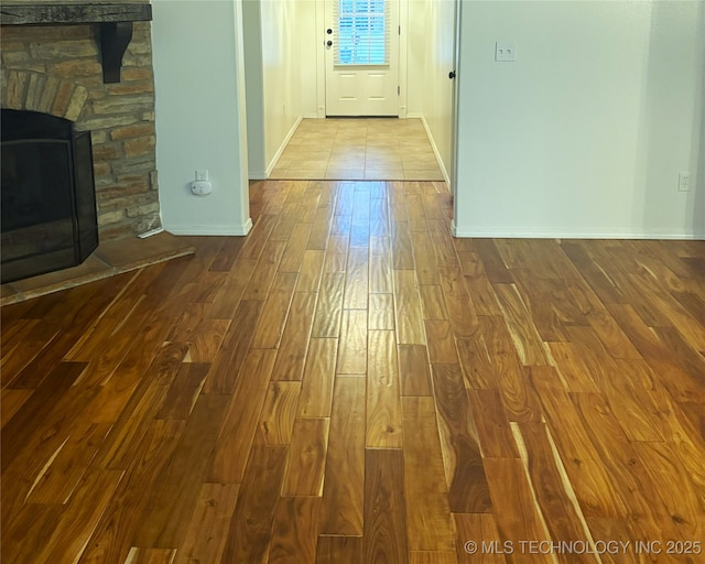 interior space with a stone fireplace, dark wood-style flooring, and baseboards