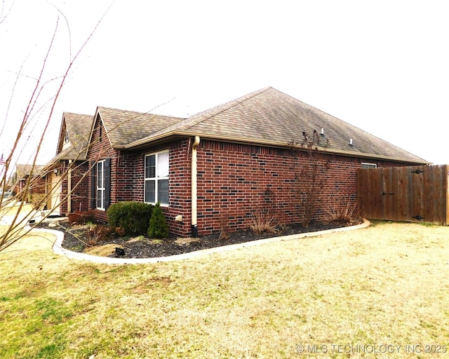 view of side of home featuring a shingled roof, fence, and brick siding