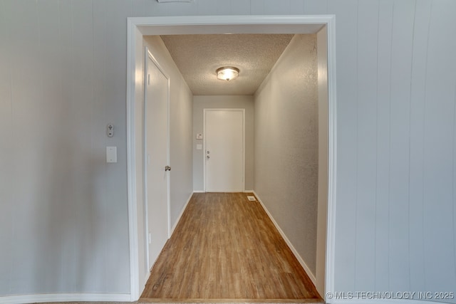 corridor featuring a textured ceiling, baseboards, and wood finished floors