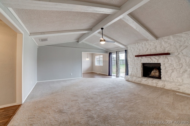 unfurnished living room featuring vaulted ceiling with beams, a textured ceiling, a stone fireplace, carpet floors, and a ceiling fan