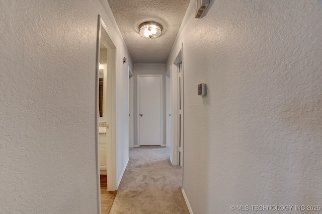 hall with light carpet, baseboards, a textured ceiling, and a textured wall