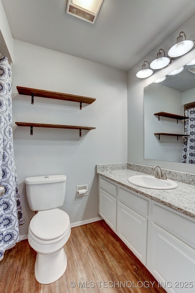 bathroom featuring visible vents, toilet, vanity, wood finished floors, and baseboards