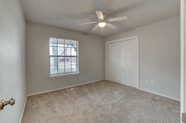 unfurnished bedroom with visible vents, a ceiling fan, carpet, a textured ceiling, and a closet