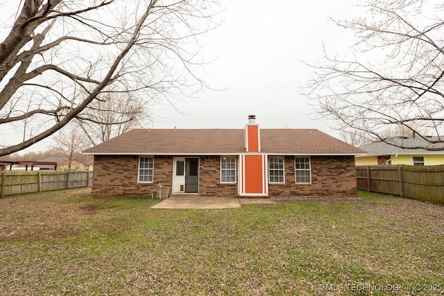 back of house with a chimney, brick siding, a yard, and a fenced backyard