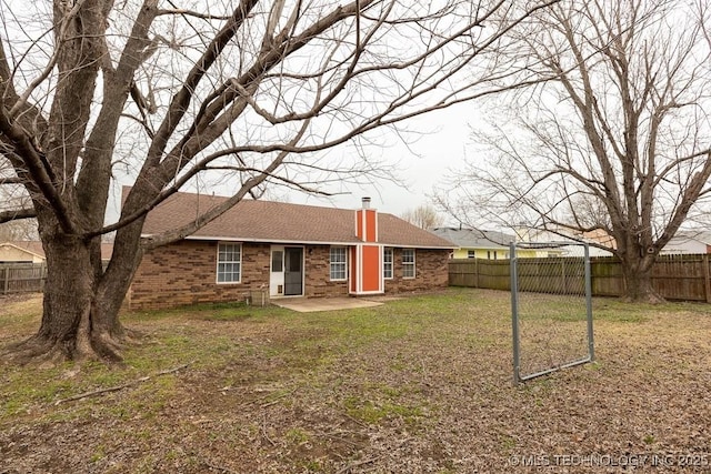 rear view of property with a fenced backyard, a chimney, a yard, a patio area, and brick siding