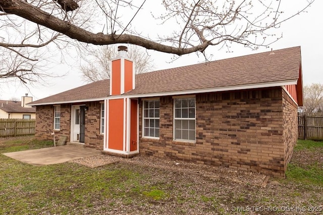 back of property featuring brick siding, fence, roof with shingles, a chimney, and a patio area