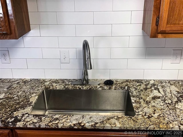 room details with tasteful backsplash, dark stone counters, brown cabinetry, and a sink