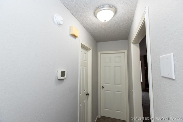 hall with a textured ceiling and a textured wall