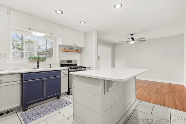 kitchen with light tile patterned floors, tasteful backsplash, blue cabinets, a sink, and gas stove