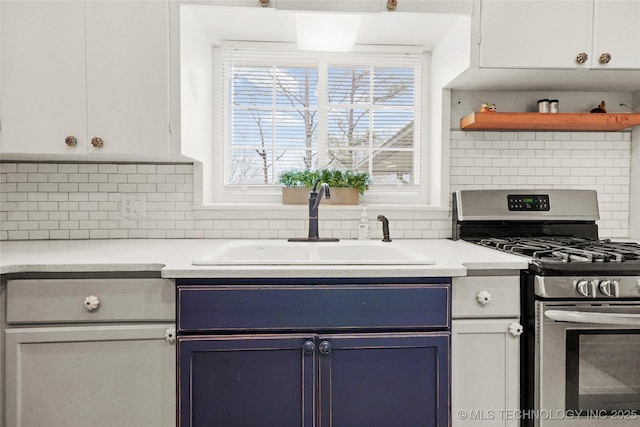 kitchen with blue cabinetry, tasteful backsplash, light countertops, stainless steel range with gas stovetop, and a sink