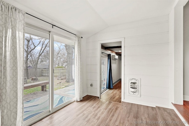 unfurnished room featuring a wall unit AC, vaulted ceiling, heating unit, and wood finished floors