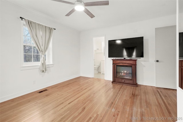 unfurnished living room featuring visible vents, a ceiling fan, a glass covered fireplace, wood finished floors, and baseboards