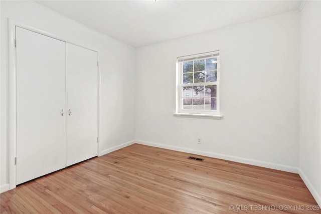 unfurnished bedroom featuring visible vents, baseboards, ornamental molding, a closet, and light wood-type flooring