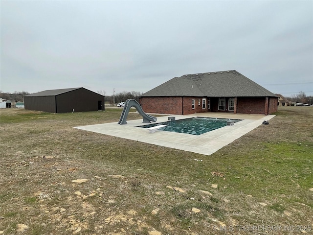 pool featuring an outbuilding, a water slide, a lawn, a pole building, and a patio area