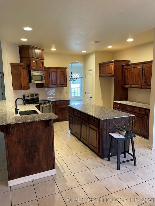 kitchen with arched walkways, stainless steel appliances, a sink, visible vents, and tasteful backsplash