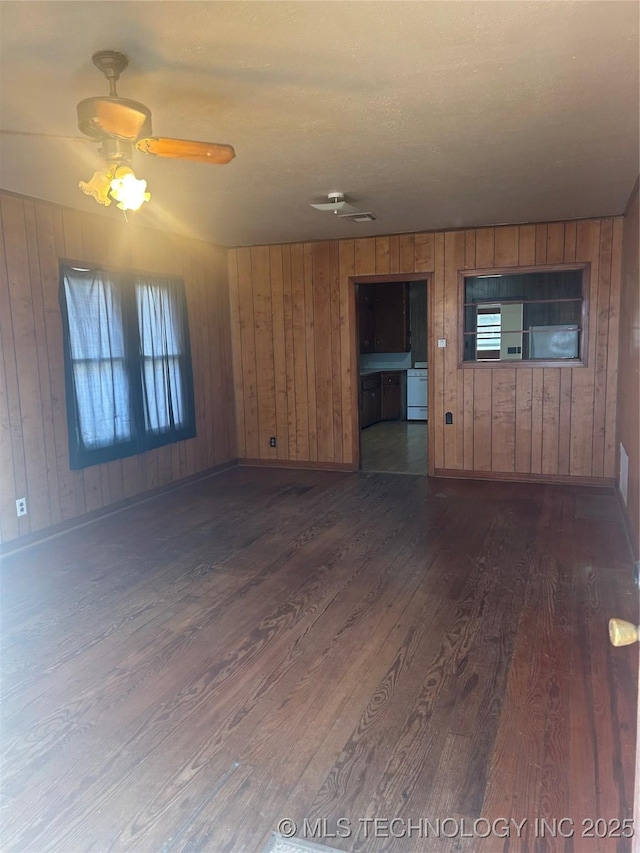 unfurnished living room featuring wood walls, a ceiling fan, baseboards, dark wood-style floors, and washer / dryer