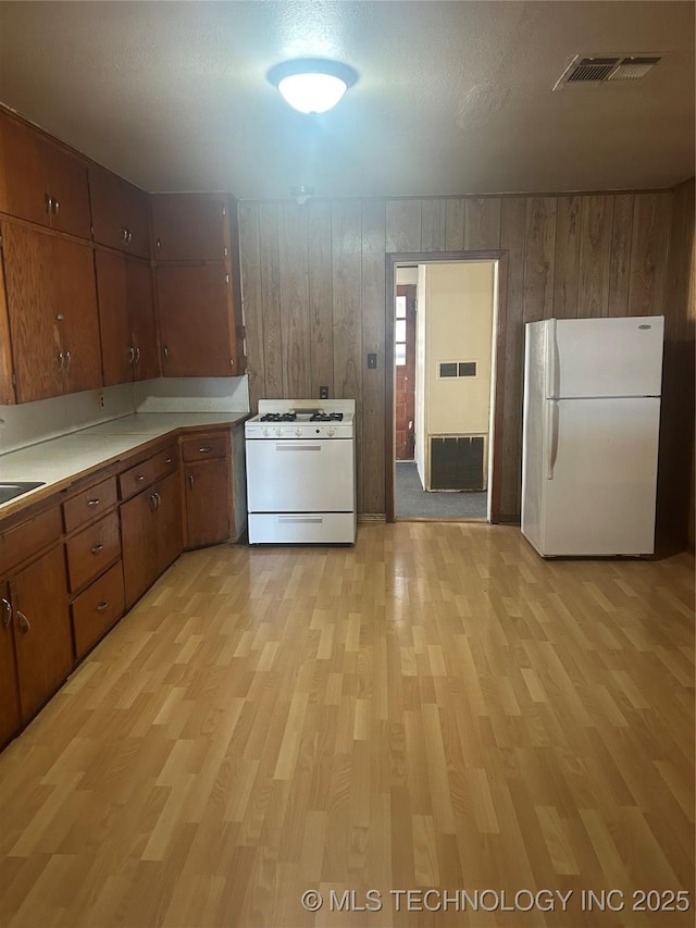 kitchen featuring brown cabinets, light wood-type flooring, white appliances, and visible vents