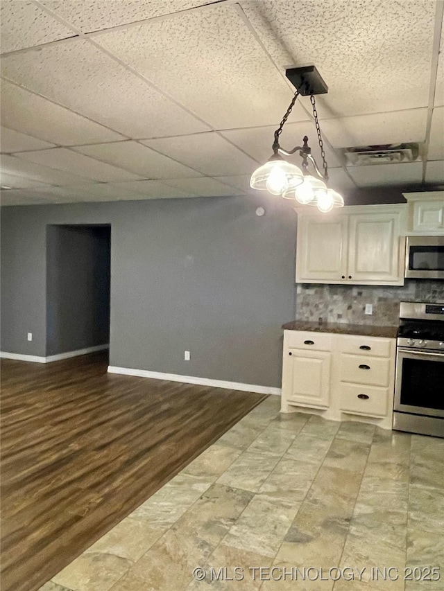 kitchen featuring baseboards, a drop ceiling, dark countertops, appliances with stainless steel finishes, and backsplash