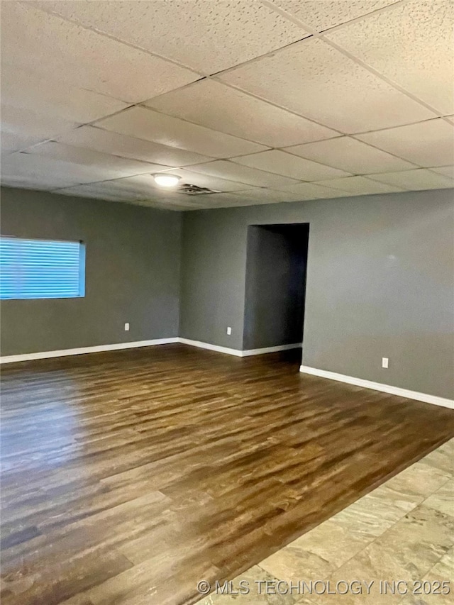 empty room featuring a drop ceiling, wood finished floors, and baseboards