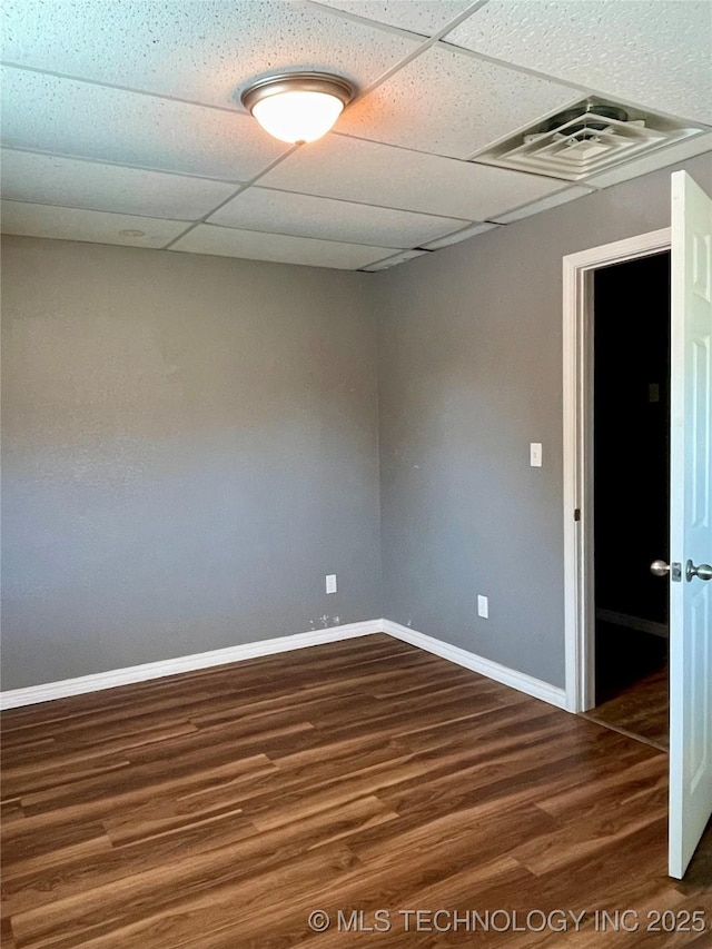 empty room with baseboards, visible vents, a drop ceiling, and wood finished floors