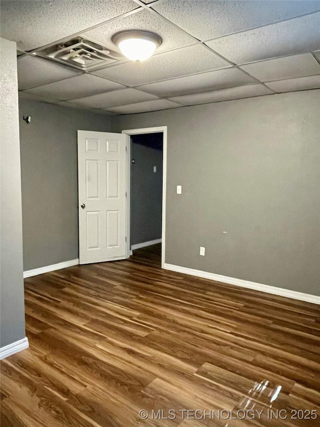 empty room featuring a paneled ceiling, visible vents, baseboards, and wood finished floors