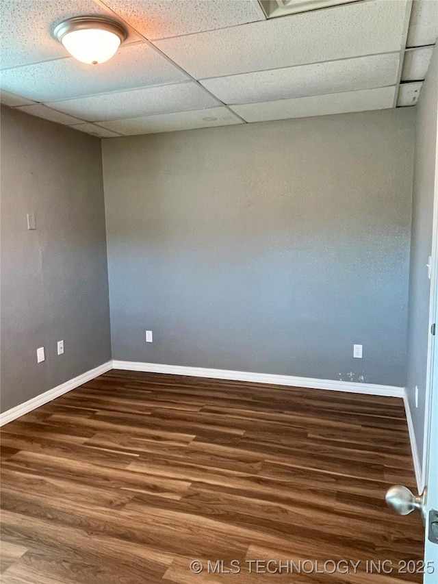 spare room with wood finished floors, a paneled ceiling, and baseboards