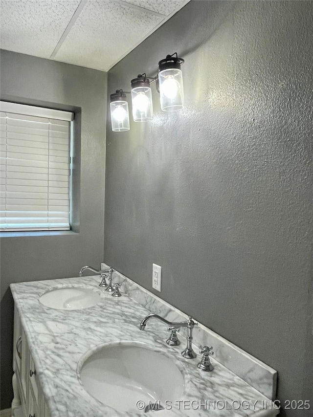 bathroom featuring a paneled ceiling, a sink, and double vanity