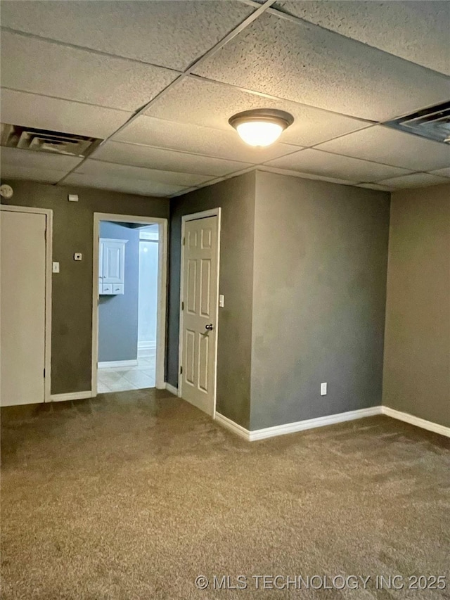 empty room with visible vents, carpet, a paneled ceiling, and baseboards