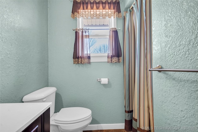 bathroom featuring baseboards, a textured wall, vanity, and toilet