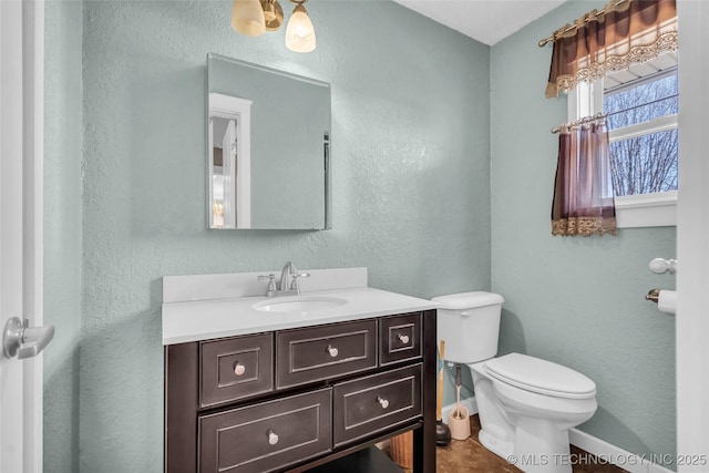 half bathroom with toilet, a textured wall, baseboards, and vanity