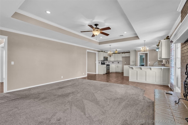 unfurnished living room featuring ceiling fan with notable chandelier, a tray ceiling, baseboards, and ornamental molding