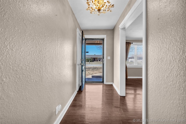 hallway featuring dark wood-style flooring, a textured wall, and baseboards