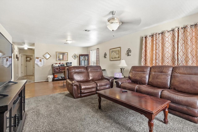 carpeted living area featuring visible vents, a ceiling fan, and wood finished floors