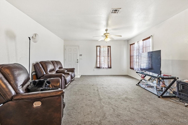 living area with carpet floors, visible vents, a wood stove, ceiling fan, and baseboards