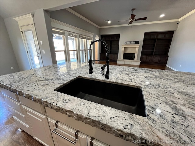 kitchen featuring a fireplace with raised hearth, open floor plan, light stone countertops, crown molding, and a sink