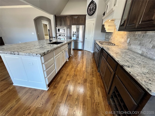 kitchen featuring arched walkways, dark brown cabinetry, stainless steel appliances, dark wood-type flooring, and a sink