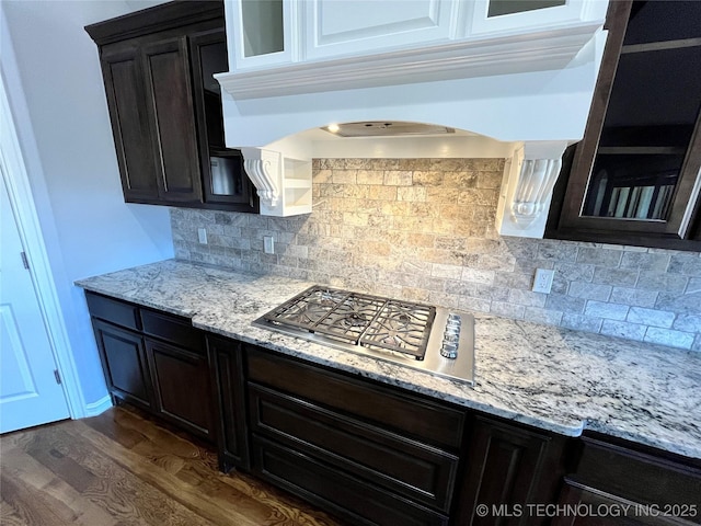 kitchen featuring dark wood finished floors, light stone counters, under cabinet range hood, stainless steel gas cooktop, and backsplash