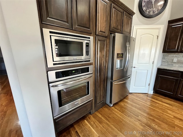 kitchen with light wood-style flooring, dark brown cabinets, appliances with stainless steel finishes, backsplash, and a warming drawer