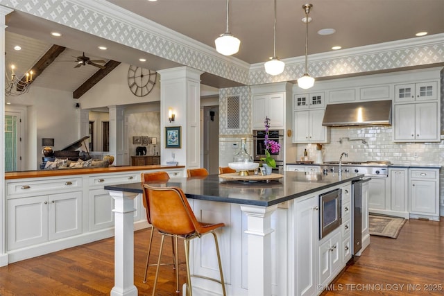 49721 E 95th Rd, Miami, OK 74354 - kitchen with under cabinet range hood, dark countertops, stainless steel appliances, white cabinets, and decorative columns