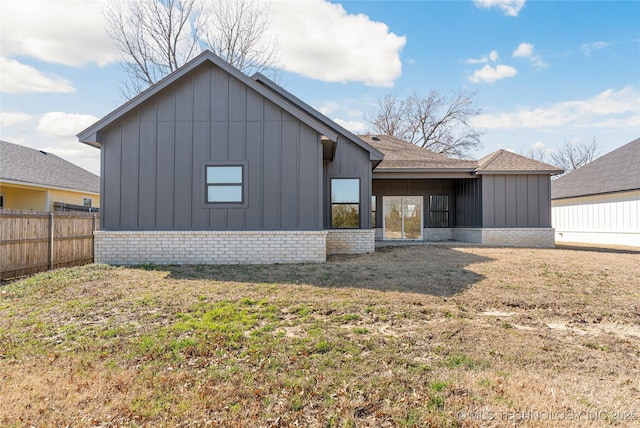 rear view of house with board and batten siding, brick siding, fence, and a lawn