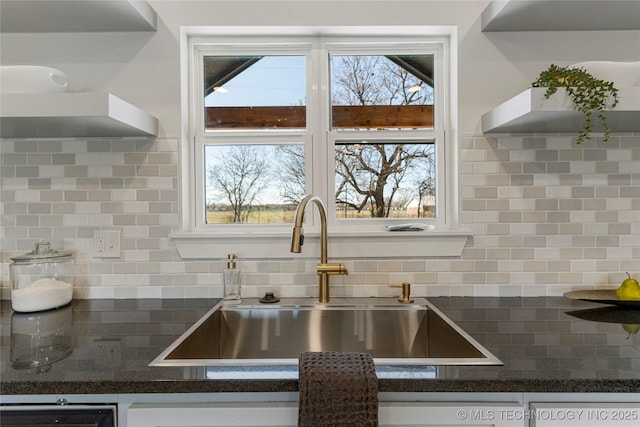 kitchen featuring open shelves, tasteful backsplash, dark countertops, and a sink