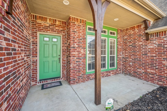 view of exterior entry with a shingled roof and brick siding