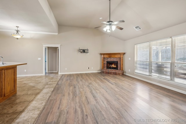 unfurnished living room with visible vents, ceiling fan, vaulted ceiling, light wood-type flooring, and a fireplace