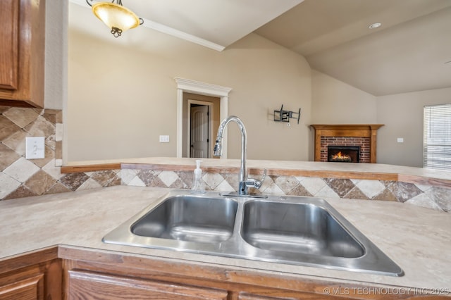 kitchen with tasteful backsplash, lofted ceiling, light countertops, a brick fireplace, and a sink